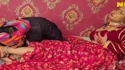 Mollige Inderin im roten Sari liegt seitlich auf dem Bett und wird von hinten von ihrem nackten Lover umarmt