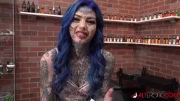 Tätowiertes Alt-Girl mit blauen Haaren und Gesichtstattoos blickt mit offenem Mund direkt in die Kamera